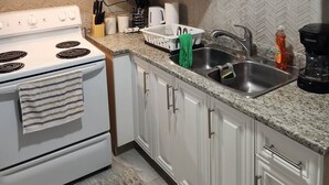 A kitchen with white cabinets, a stove, a sink, and a herringbone-patterned backsplash.