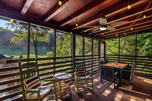 A covered outdoor seating area with wooden benches and tables, overlooking a lush green landscape.