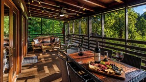 An outdoor patio with a wooden deck, wicker furniture, and a table set with food and drinks.