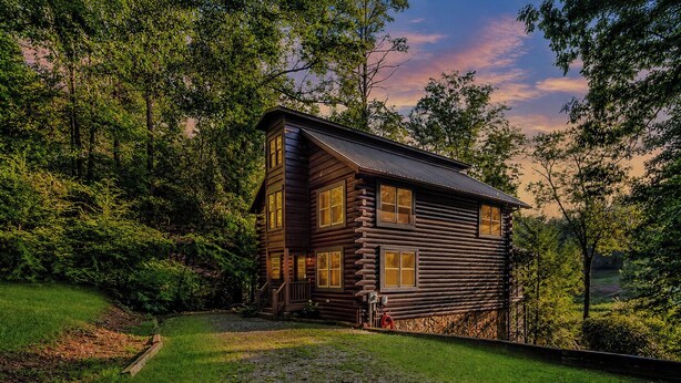 A log cabin with a porch and a gravel driveway.