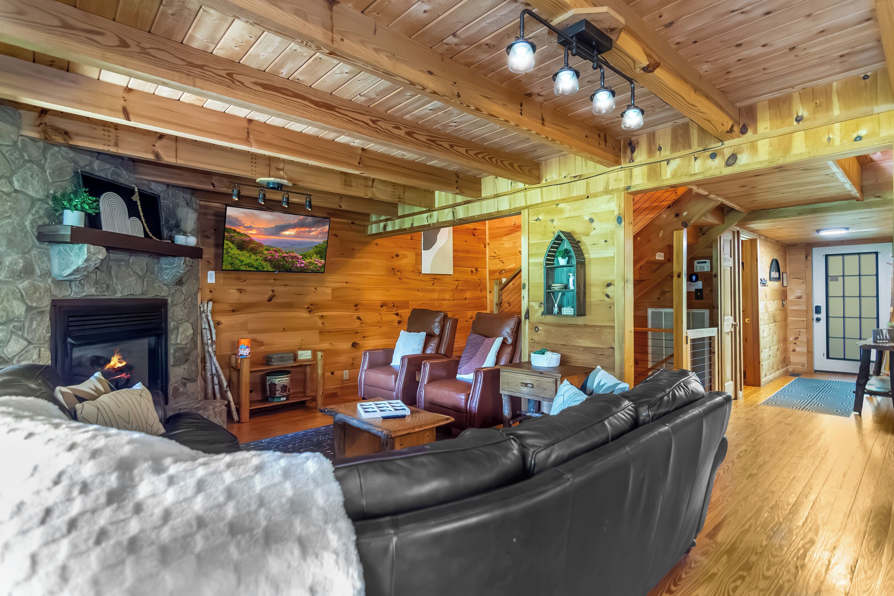 L’intérieur d’un chalet confortable, avec une cheminée, des fauteuils en cuir, un téléviseur et un mur en pierre.