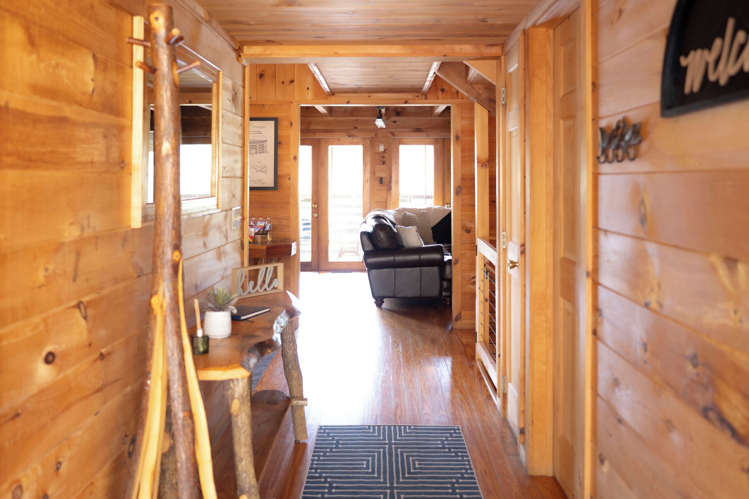 A wooden cabin interior with a sofa, a welcome sign, and a framed picture on the wall.