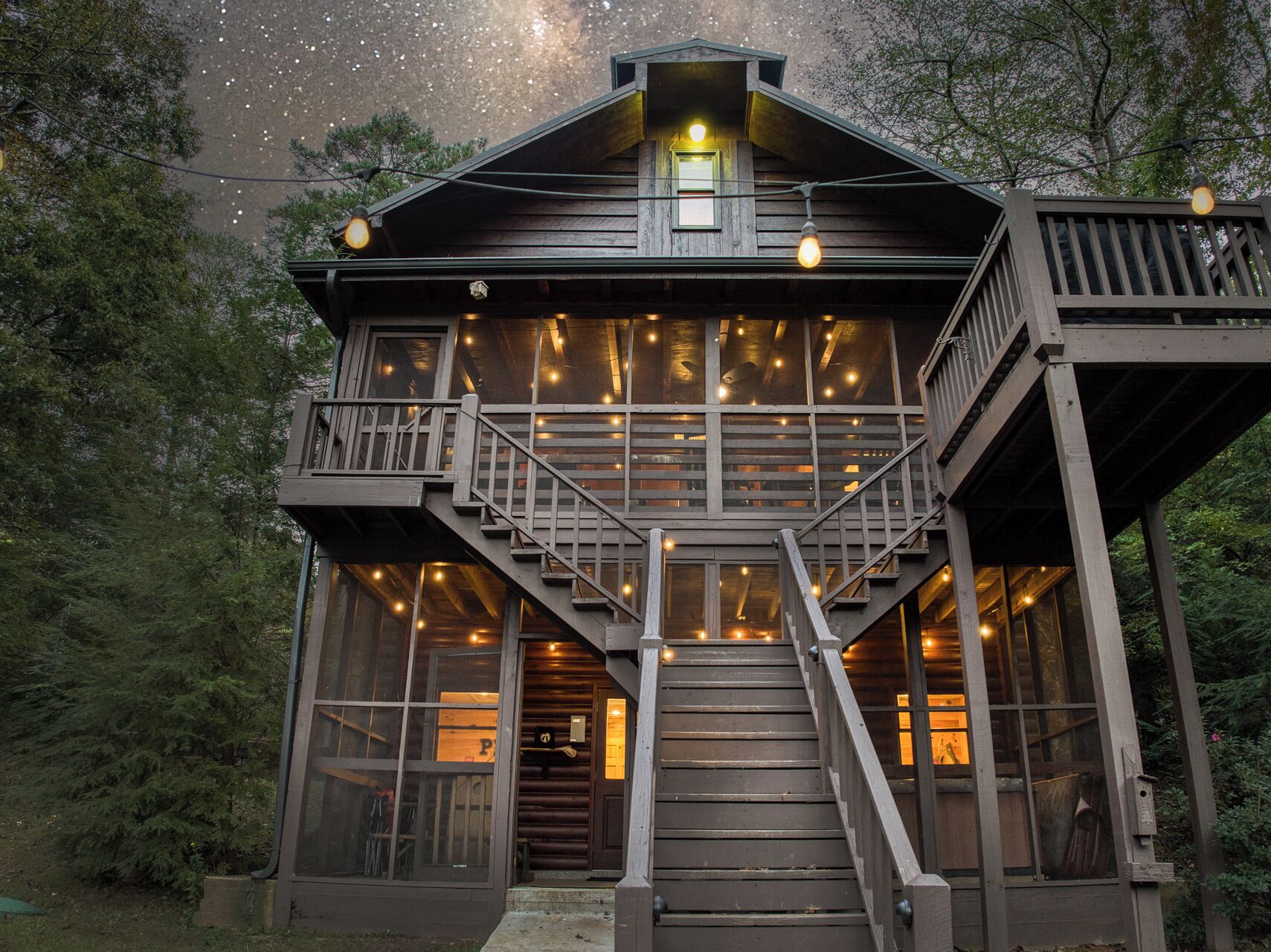 A wooden cabin with a balcony, large windows, and a staircase leading to the upper level.