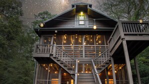 A wooden cabin with a balcony, large windows, and a staircase leading to the upper level.
