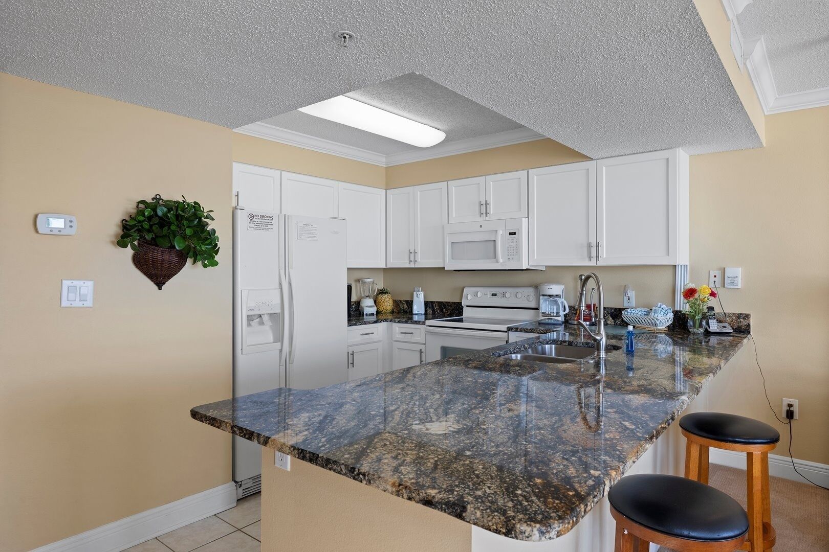 A modern kitchen with white cabinets, a granite countertop, a built-in microwave, and a stainless steel sink.