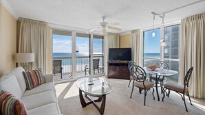 A hotel room with a balcony, a sofa, a dining table, and a TV. - Pelican Beach 0411 1 Bedroom Condo by Pelican Beach Management (Destin)