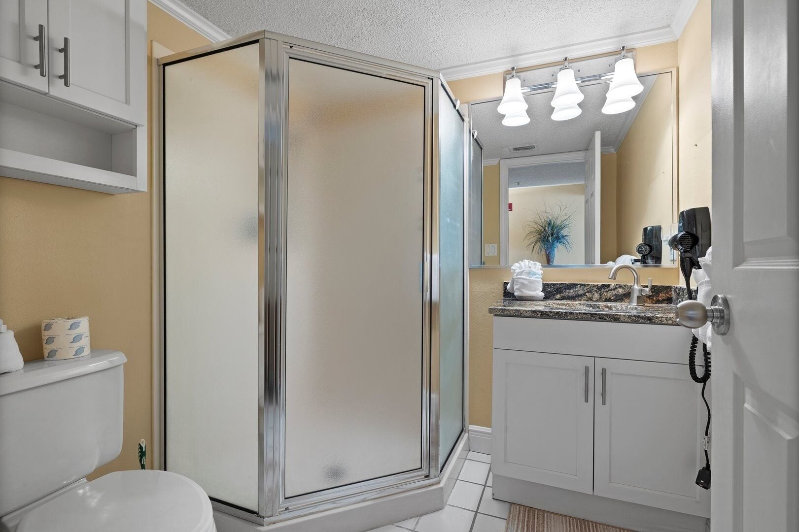 A modern bathroom with a glass-enclosed shower, a white sink with a granite countertop, and a mirror above the sink.