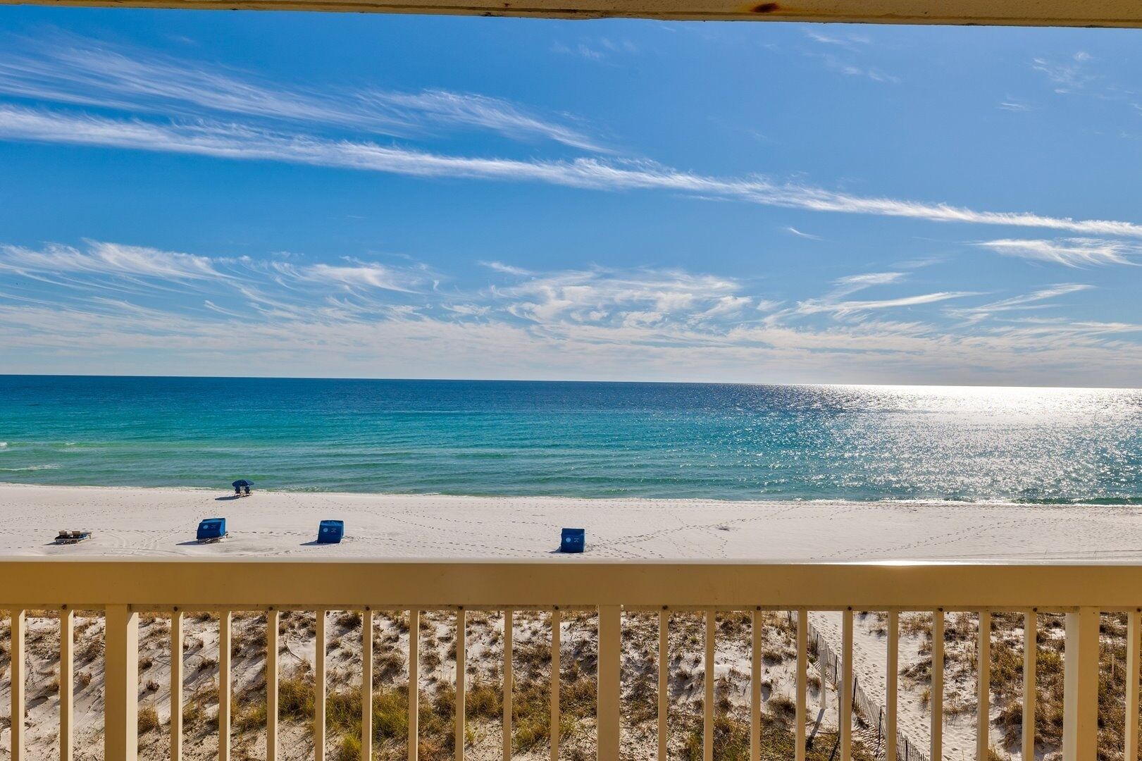 Une vue sur la plage depuis un balcon doté d’une balustrade, avec une plage de sable et l’océan en toile de fond.