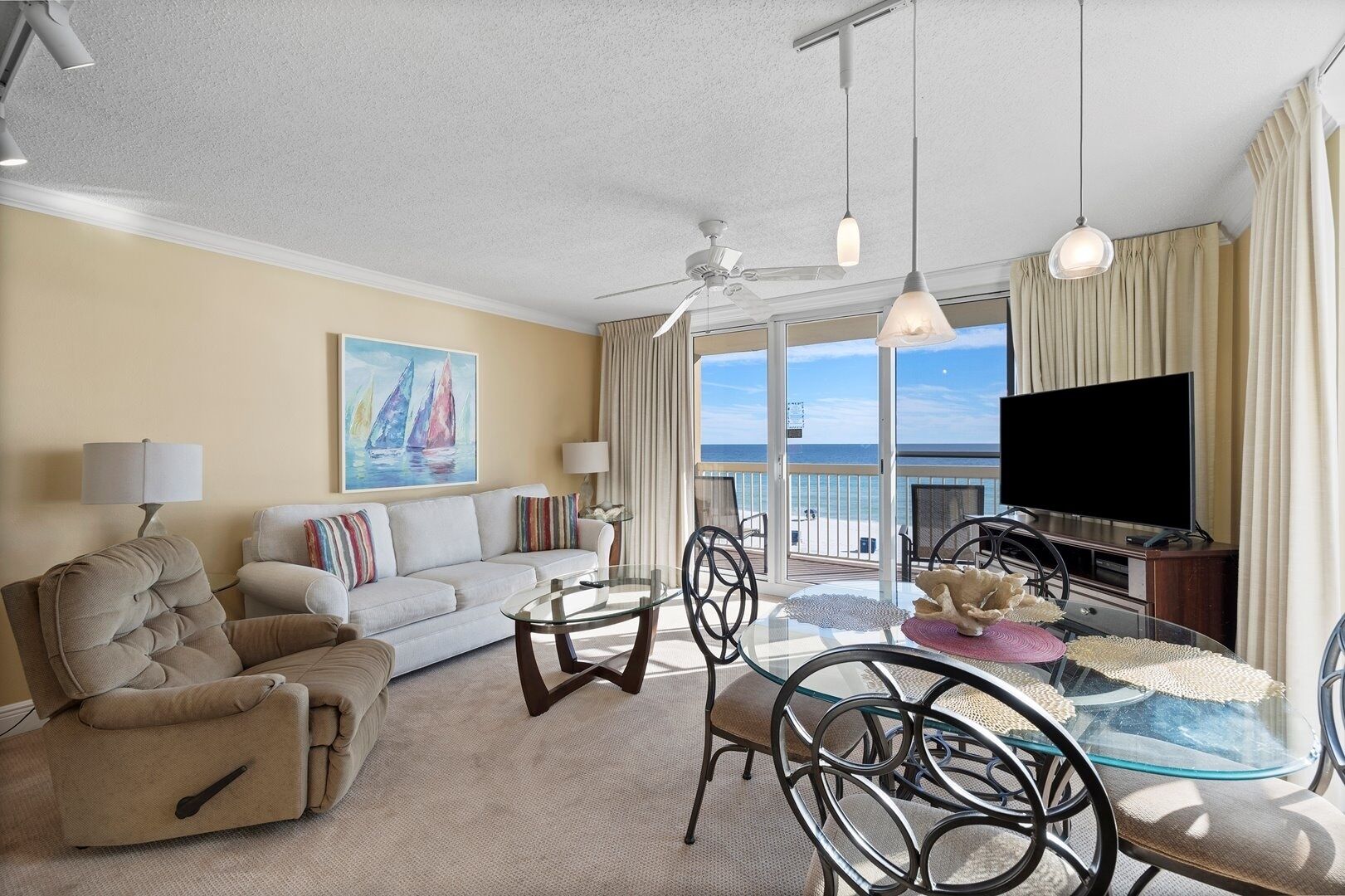 A living room with a sofa, armchair, glass coffee table, and a TV.