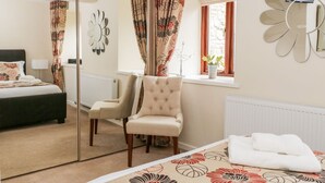 Ein Schlafzimmer mit Bett, Sessel, Spiegel und einem fenster mit Vorhängen.