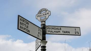 A directional signpost with multiple arms pointing to various destinations such as Airton, Settle, Skipton, Gorda, Malham Tarn, and Malham.