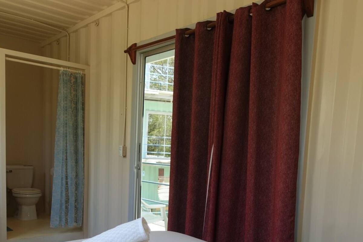 A hotel room with a bed, a window with red curtains, and a view of an outdoor area.