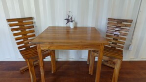 A wooden dining table with two chairs, a small white vase with a plant, and a white wall with vertical lines in the background. - Casa Maya Eco Lodge (San Juan del Sur)