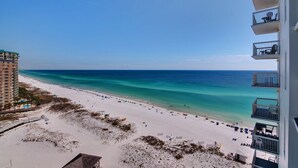 A beach view with a clear sky, a sandy shore, and a building with balconies overlooking the beach. - Pelican Beach 1512 2 Bedroom Condo by Pelican Beach Management (Destin)