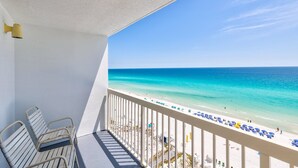 A balcony with a view of a beach, white railings, and a few chairs. - Pelican Beach 1206 1 Bedroom Condo by Pelican Beach Management (Destin)