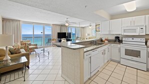 A modern hotel room with a kitchen, dining area, and a balcony with ocean views. - Pelican Beach 1206 1 Bedroom Condo by Pelican Beach Management (Destin)
