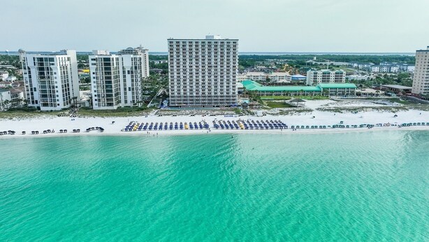 A coastal cityscape with a beach, high-rise buildings, and a clear turquoise sea. - Pelican Beach 1716 2 Bedroom Condo by Pelican Beach Management (Destin)