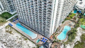 A high-rise hotel with multiple balconies, two swimming pools, and a landscaped area with sun loungers. - Pelican Beach 1716 2 Bedroom Condo by Pelican Beach Management (Destin)