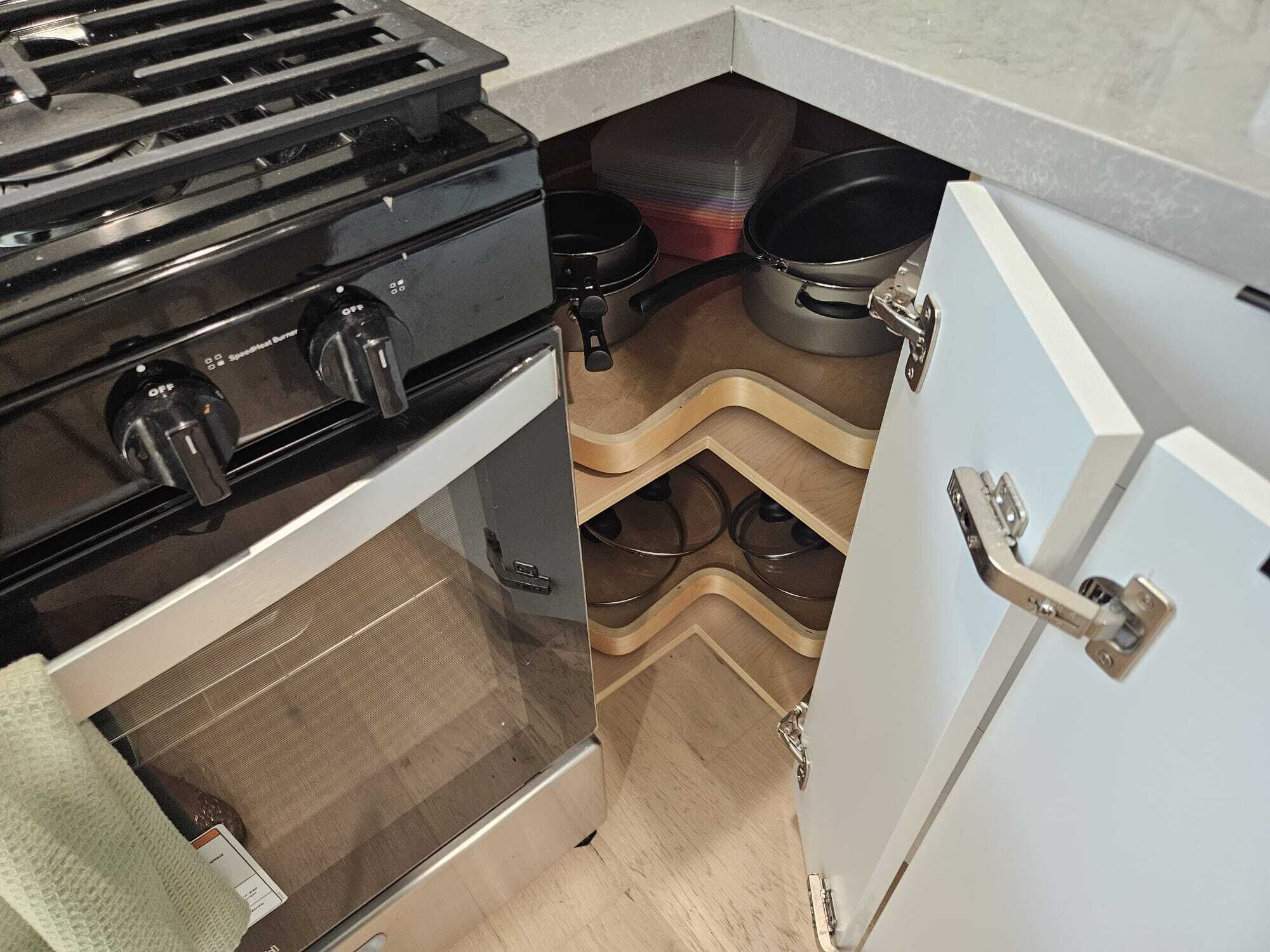 A compact kitchen with a stove, pots, and a white cabinet.