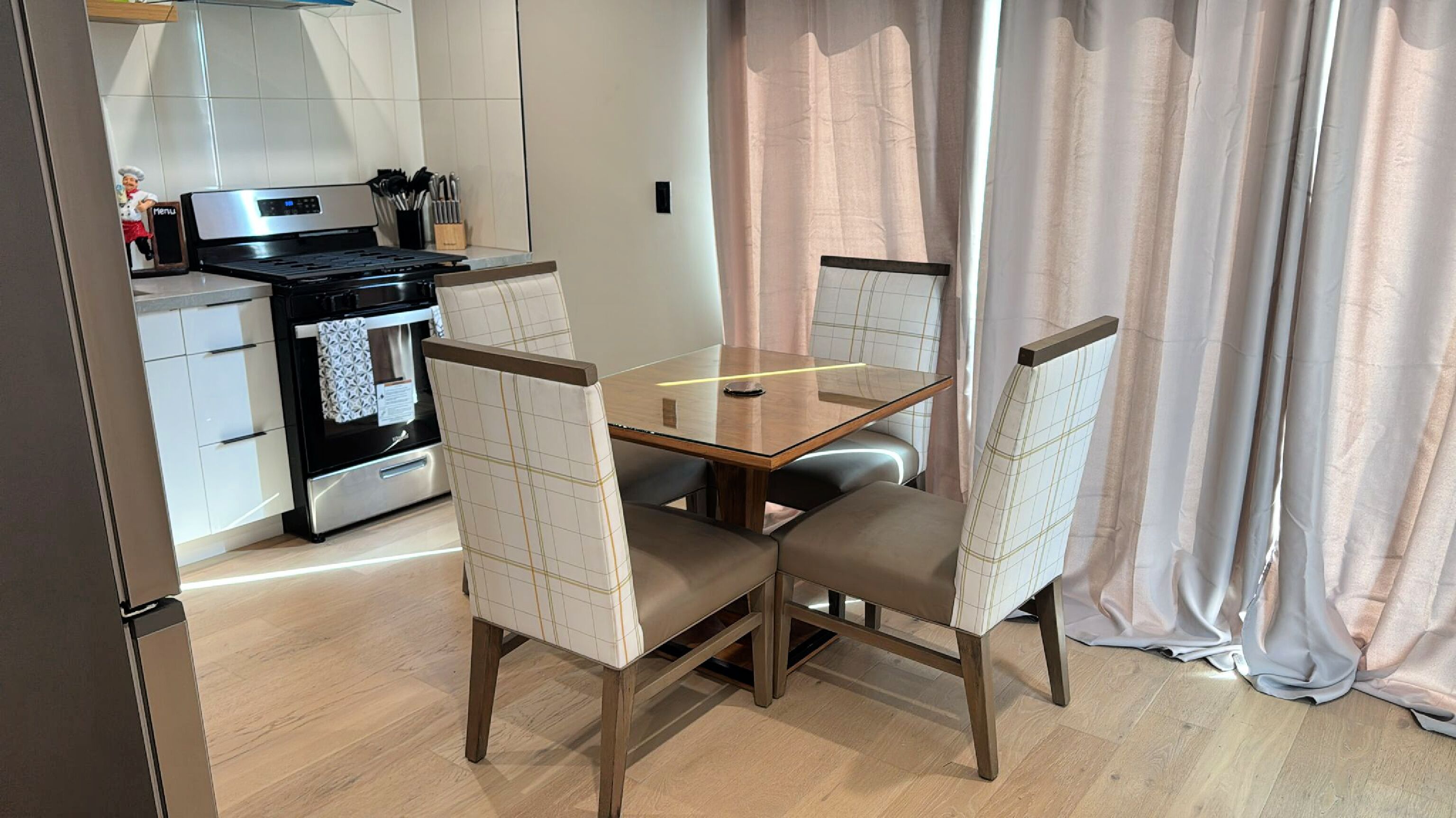 A modern kitchen with a built-in oven, a stove, and a dining area with a glass table and cushioned chairs.
