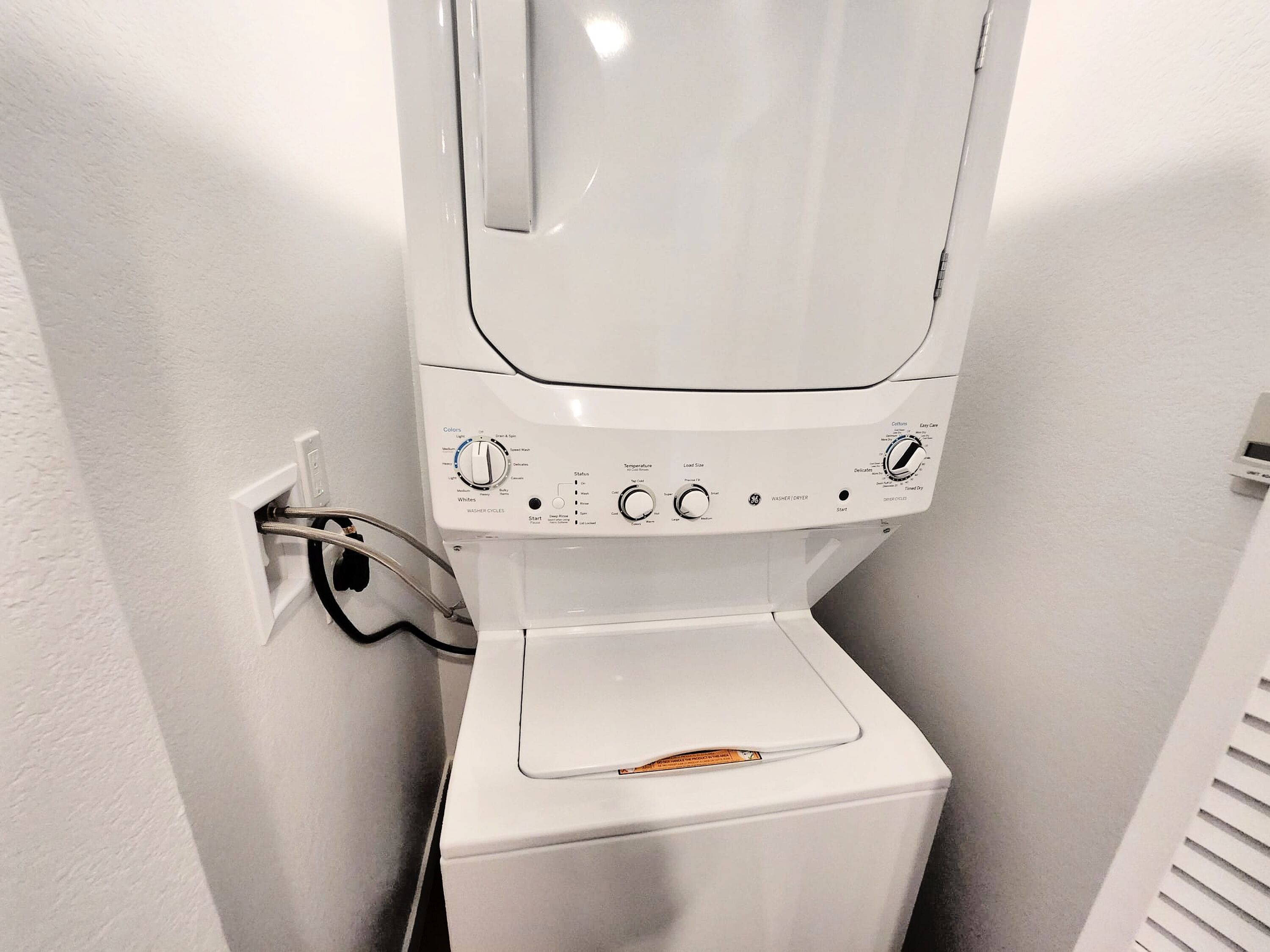 A front-loading washing machine with control panel, water inlet hose, and a safety lock on the door.