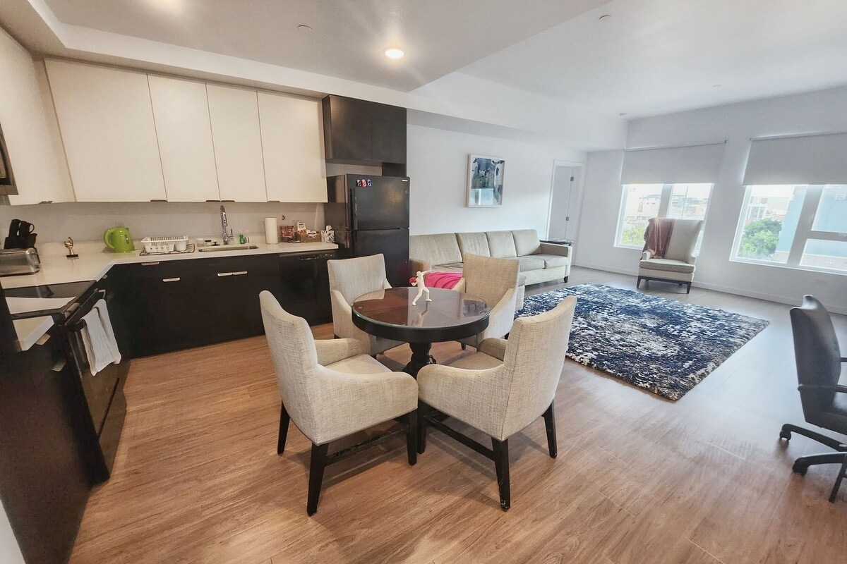 A modern kitchen with dark cabinets, a dining table with four chairs, and a large window providing natural light.