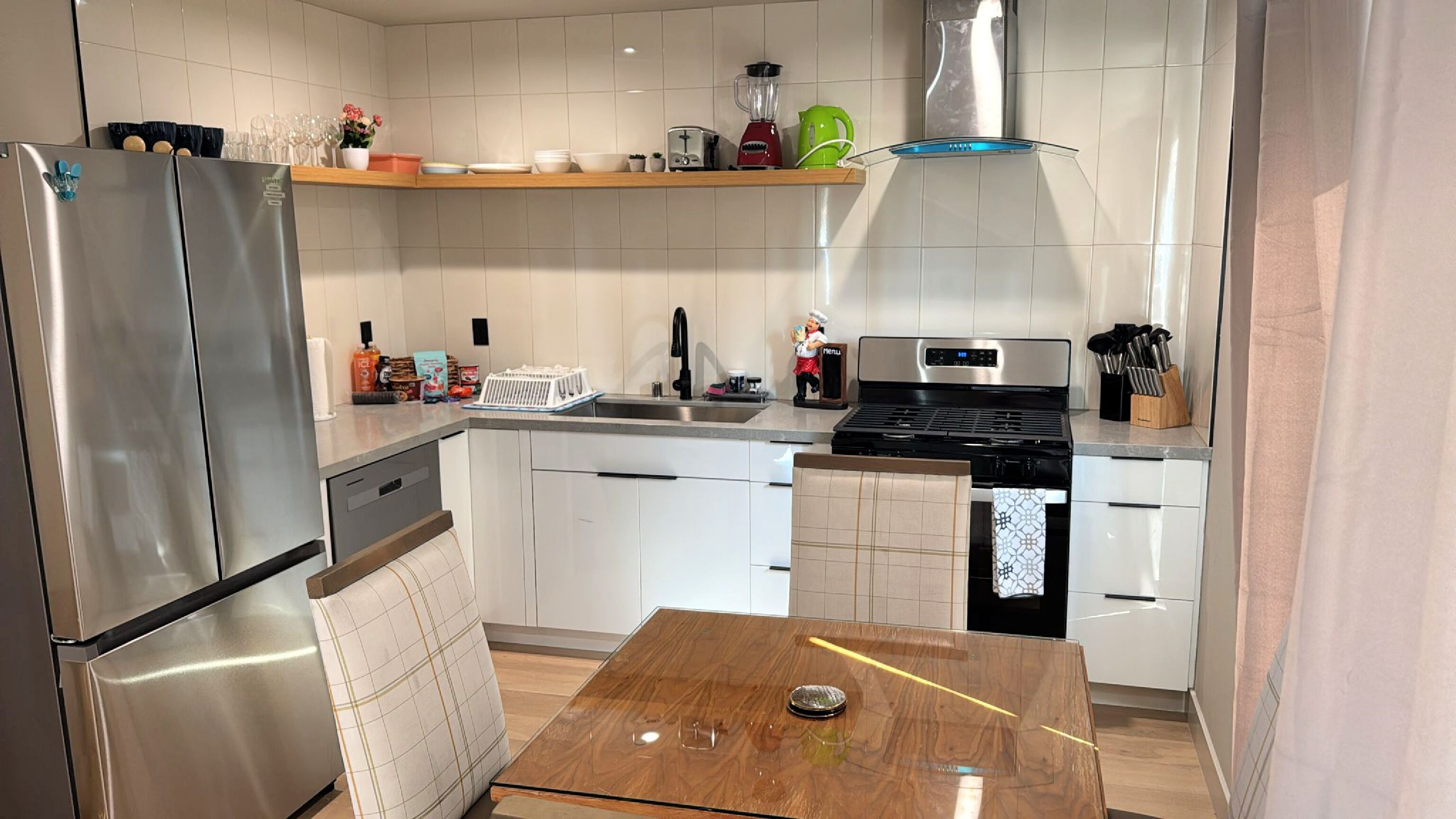 A compact kitchen with white cabinets, a stainless steel refrigerator, a wooden table, and a built-in stove.