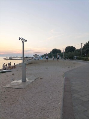 En strand med folk, der spiller volleyball, et livreddertårn og både i baggrunden.