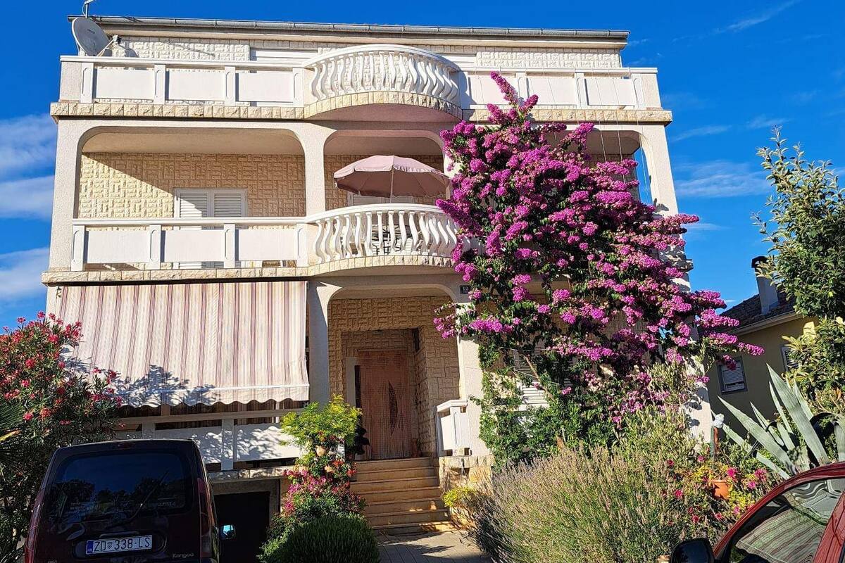 A two-story building with a balcony, a driveway, and parked cars.