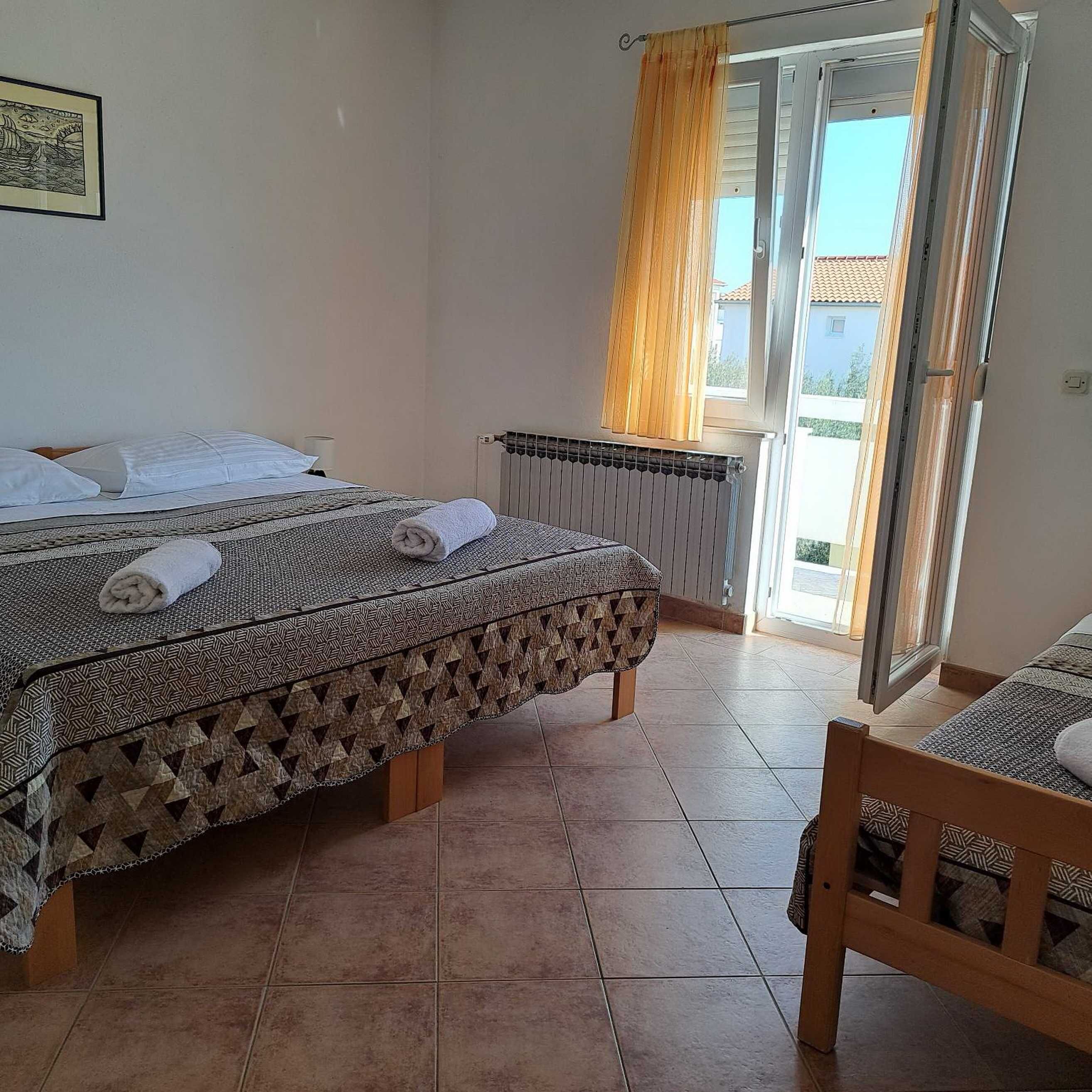 A bedroom with a bed, a chair, a radiator, and a window with curtains.