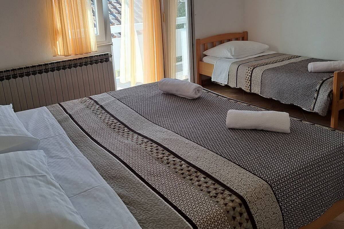 A hotel room with two single beds, a window with curtains, a radiator, and a painting on the wall.