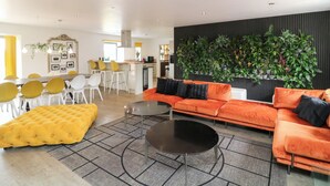 A modern living room with a sofa, ottoman, and coffee table. There is a dining area with chairs and a table. A kitchen is visible in the background. - Hayloft (Lincoln)