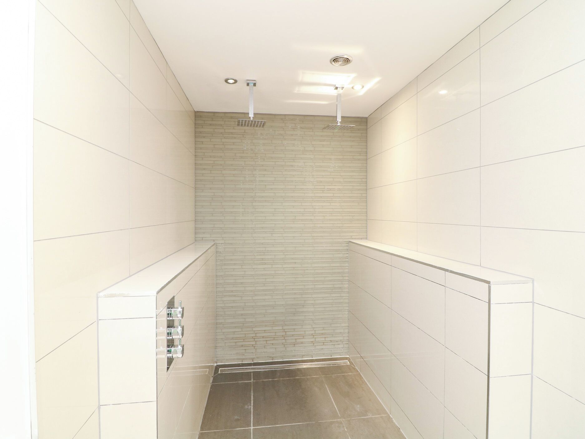 A narrow, tiled shower with a brick wall and a white ceiling.