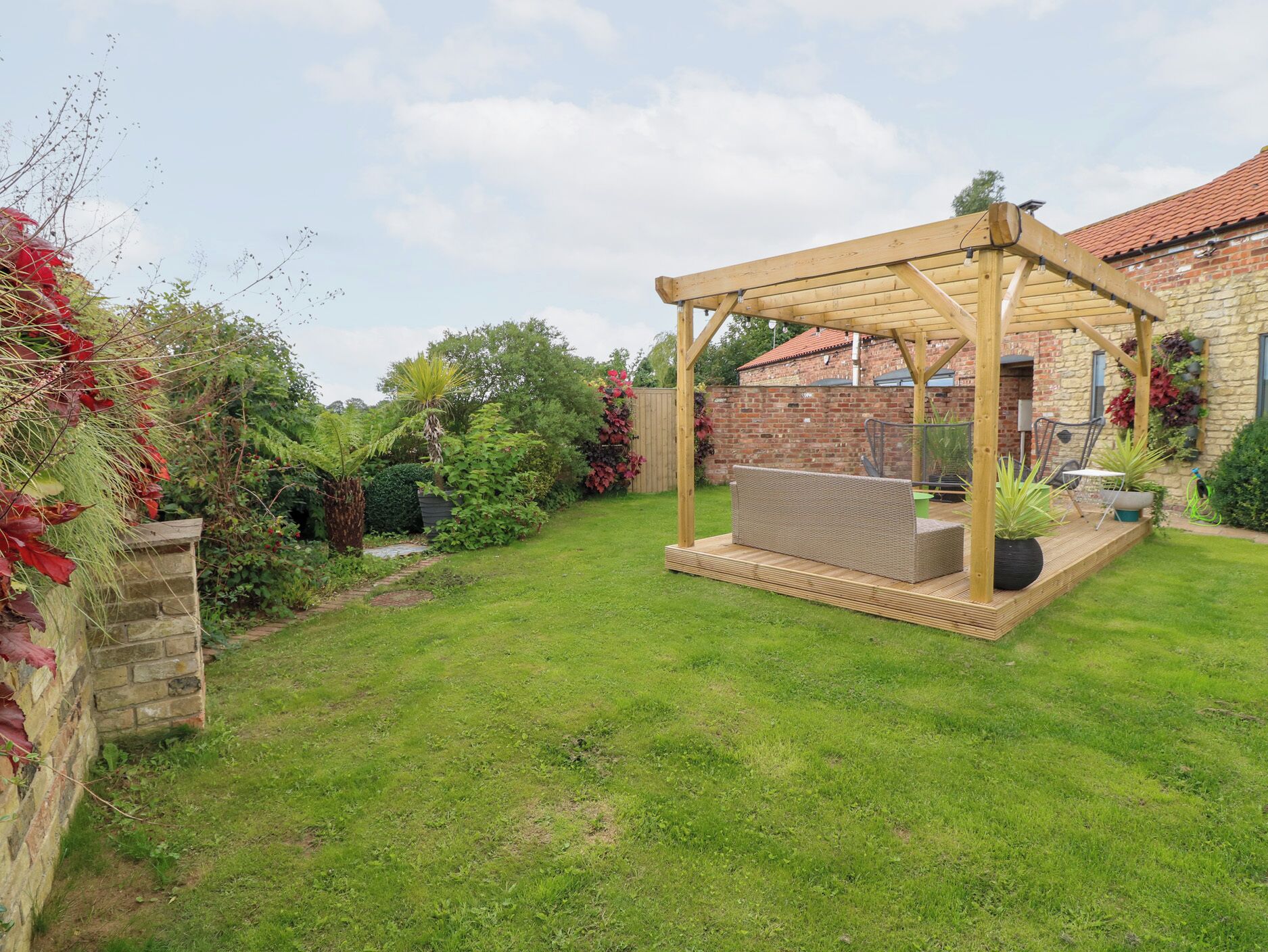 A covered patio area with a wooden pergola, a wicker sofa, and potted plants.