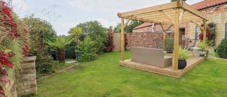 A covered patio area with a wooden pergola, a wicker sofa, and potted plants.