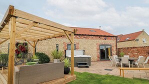 A covered outdoor seating area with a wooden pergola, a hot tub, and a stone building with a tiled roof. - Hayloft (Lincoln)