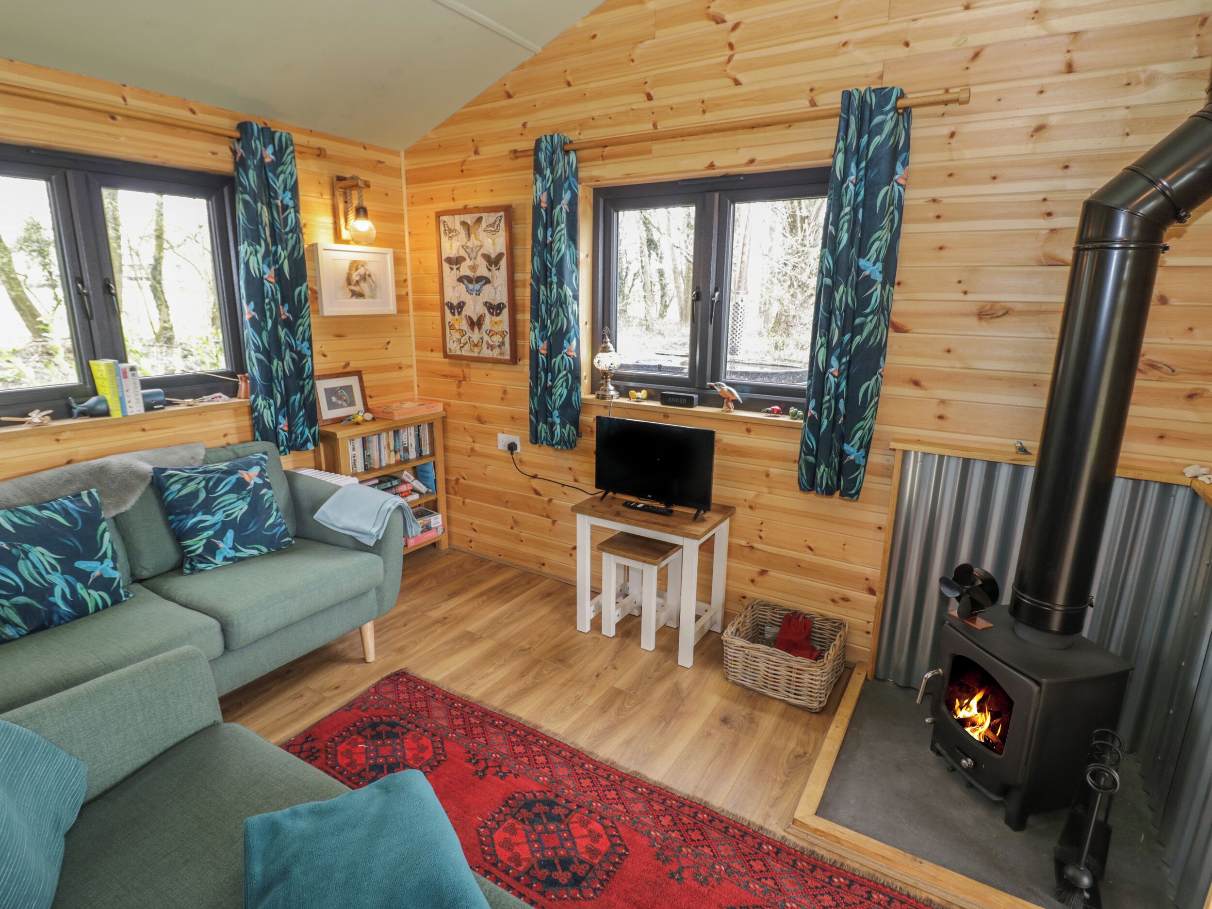 Ein gemütliches Blockhaus-Interieur mit Sofa, Fernseher, Bücherregal und Kaminofen.