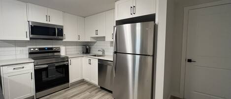 A modern kitchen with white cabinets, stainless steel appliances, and a wooden floor.