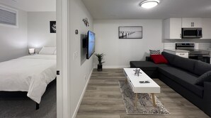 Ein modernes, kompaktes Wohnzimmer mit Bett, Sofa, Fernseher, Küchenzeile und Esstisch.