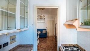 A narrow hallway with a blue sofa, a chandelier, and a kitchen area with a gas stove.