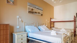 A bedroom with two beds, a nightstand, a wooden wardrobe, and a painting on the wall.