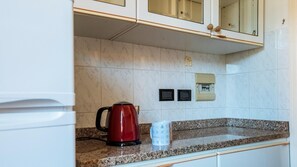 A kitchen with white cabinets, a granite countertop, a red kettle, and a coffee mug.