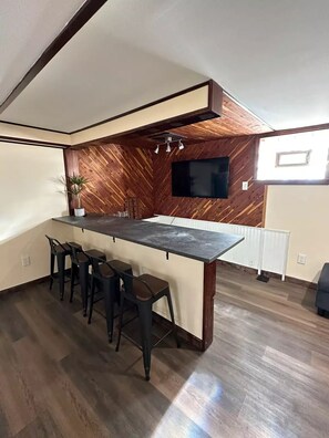 Cozinha moderna com uma ilha grande, banquetas de bar, televisão na parede e painéis de madeira.
