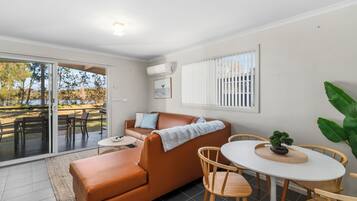 A modern living room with a brown leather sofa, a small round table, and a dining area with wooden chairs.