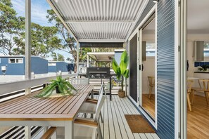 A covered outdoor deck with wooden furniture, a grill, and a potted plant.