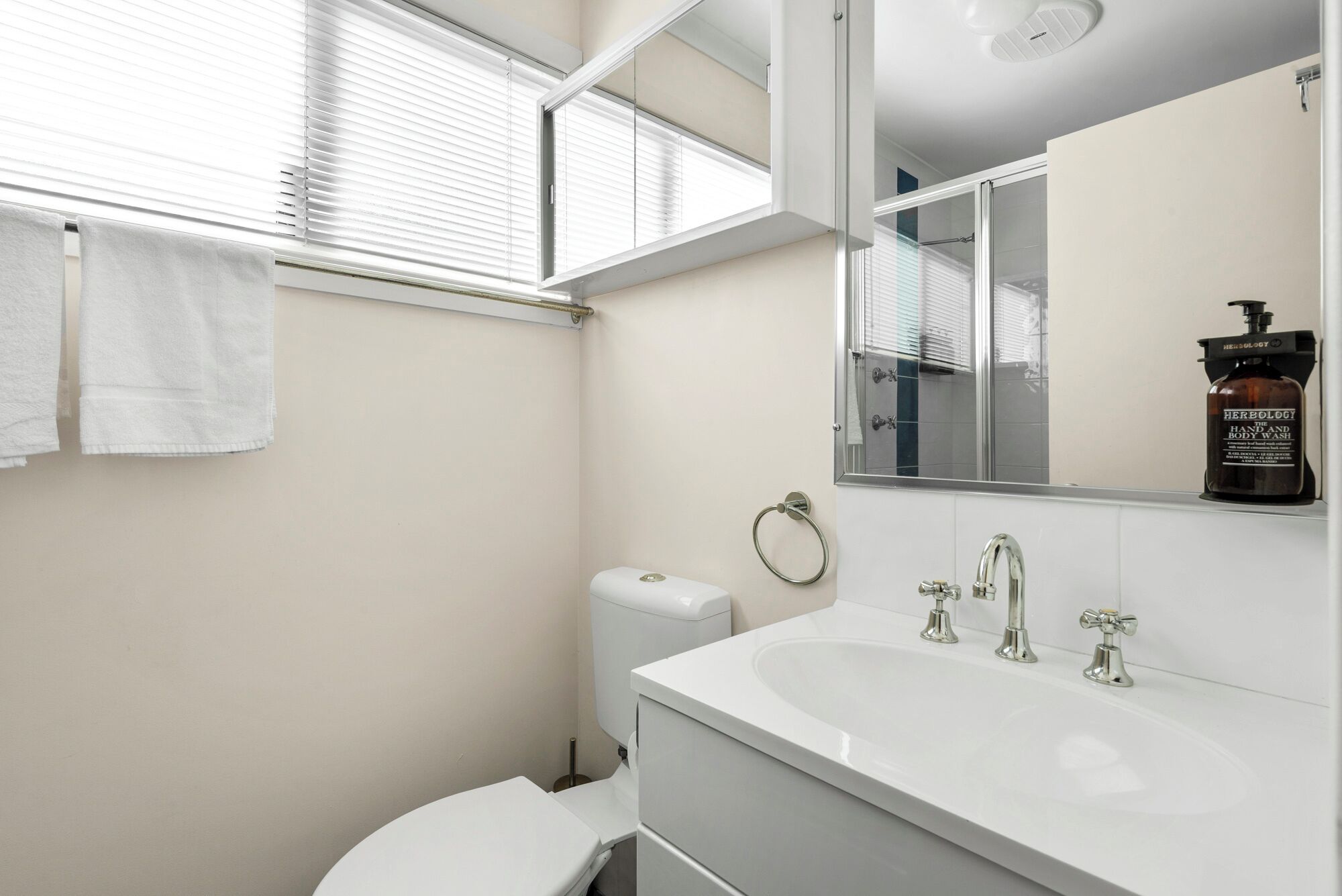 A modern bathroom with a white sink, two faucets, a toilet, and a towel rack with two towels.