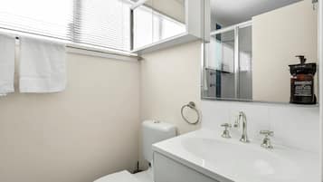 A modern bathroom with a white sink, two faucets, a toilet, and a towel rack with two towels.