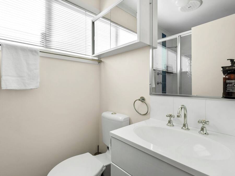 A modern bathroom with a white sink, two faucets, a toilet, and a towel rack with two towels.