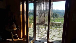 A room with a sliding glass door leading to a stone patio with a bench and a view of a vineyard.