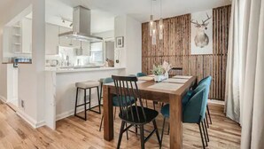 Une cuisine moderne avec des armoires blanches, une hotte en acier inoxydable et un coin repas comprenant une table en bois et des chaises bleues.